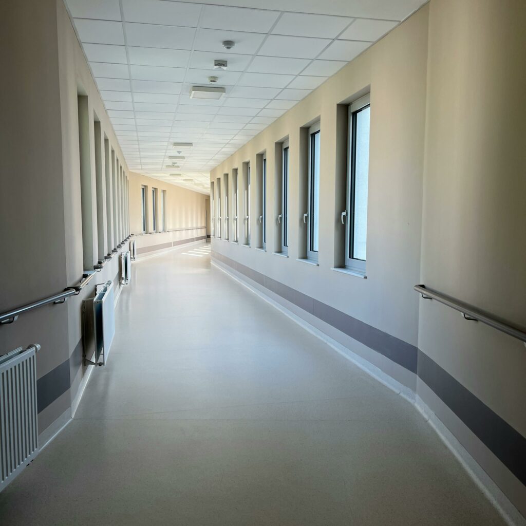 A modern, empty hospital corridor with large windows and handrails, well-lit and inviting.