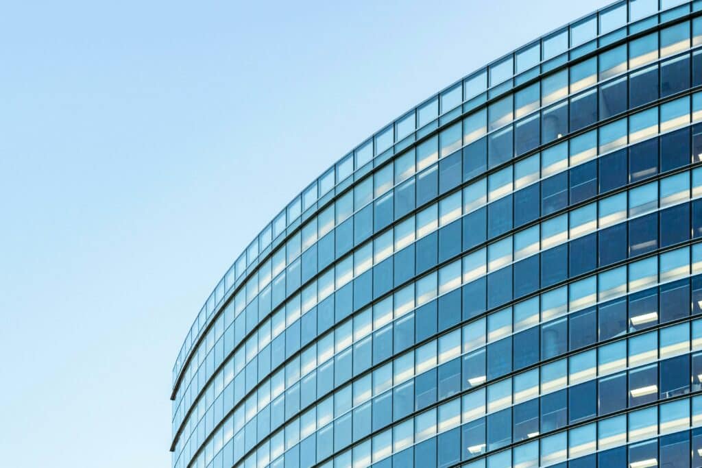 Low angle view of a modern glass office building against a clear blue sky.